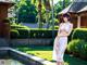 A woman in a white dress standing next to a pool.