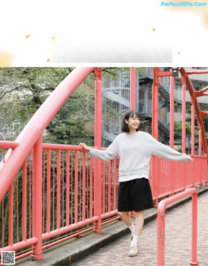 A woman standing on a red bridge with her arms outstretched.