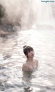 A woman is standing in the water in front of a waterfall.