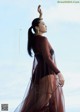 A woman in a long brown dress standing on a beach.